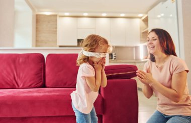 Gözleri bağlı oyun oynuyorlardı. Genç bir anne ve küçük kızı evde birlikte günlük kıyafetler giyiyorlar..