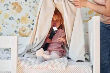 El feneriyle battaniyenin altında oturmak. Gündüz vakti evde rahat giyimli şirin küçük bir kız var..