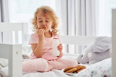 Kurabiye yiyerek kahvaltı yapmak. Gündüz vakti evde rahat giyimli şirin küçük bir kız var..