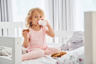 Kurabiye yiyerek kahvaltı yapmak. Gündüz vakti evde rahat giyimli şirin küçük bir kız var..