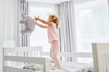 Yastıkla oynayıp fırlatıyorsun. Gündüz vakti evde rahat giyimli şirin küçük bir kız var..