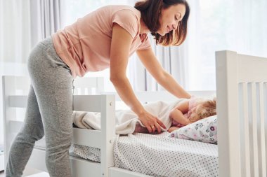 Sleep time. Young mother with her little daughter in casual clothes together indoors at home.