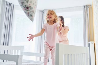 Yastık fırlatarak eğleniyorum. Genç bir anne ve küçük kızı evde birlikte günlük kıyafetler giyiyorlar..