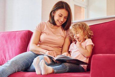 Büyük kitap okuyorum. Genç bir anne ve küçük kızı evde birlikte günlük kıyafetler giyiyorlar..