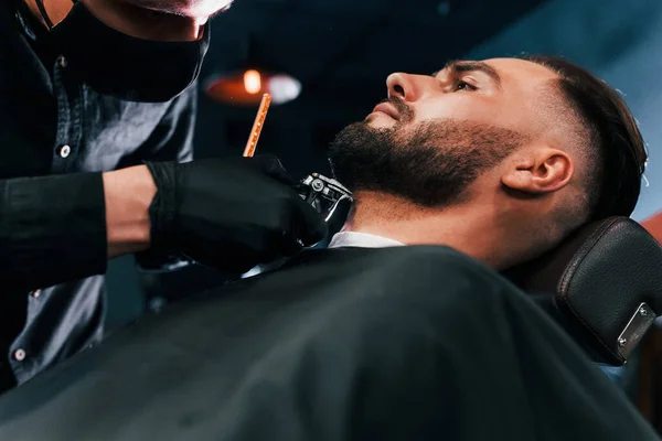 理发店里 身穿黑色防护面具的年轻人坐着刮胡子 留着时髦的发型 — 图库照片