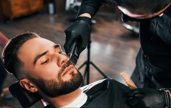 Jovem Com Penteado Elegante Sentado Recebendo Sua Barba Raspada Barbearia — Fotografia de Stock