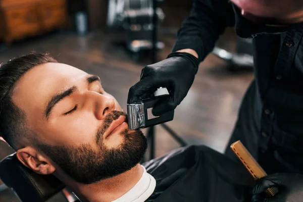理发店里 身穿黑色防护面具的年轻人坐着刮胡子 留着时髦的发型 — 图库照片