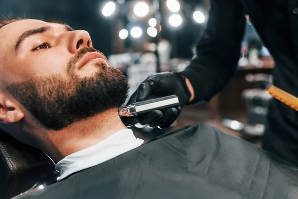 Jovem Com Penteado Elegante Sentado Recebendo Sua Barba Raspada Barbearia — Fotografia de Stock