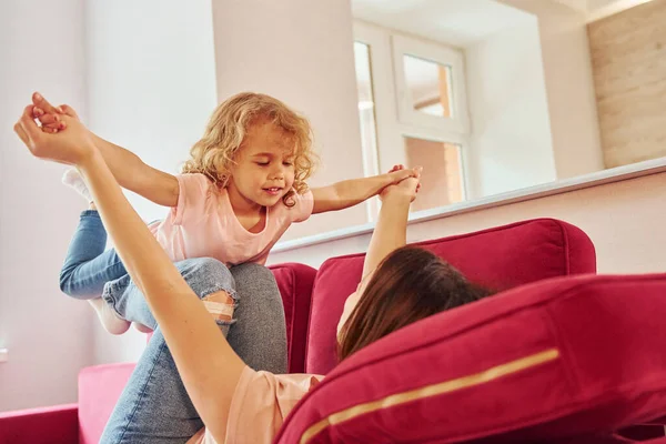 Kırmızı kanepede eğleniyorum. Genç bir anne ve küçük kızı evde birlikte günlük kıyafetler giyiyorlar..