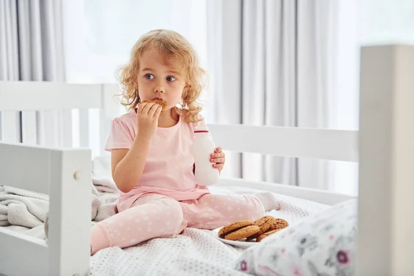 クッキーを食べて朝食をとる カジュアルな服のかわいい女の子は昼間家にいます — ストック写真