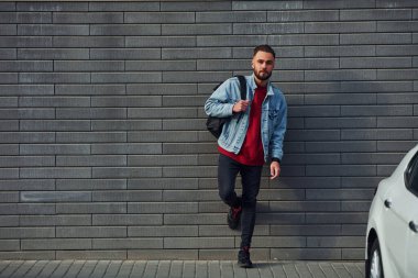 Günlük kıyafetlerle yakışıklı genç adam güneşli bir günde dışarıda, beyaz arabanın yanında..