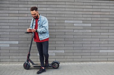 Gündüz vakti elektrikli ayakkabıyla dışarıda dikilen, günlük kıyafetli yakışıklı bir genç..