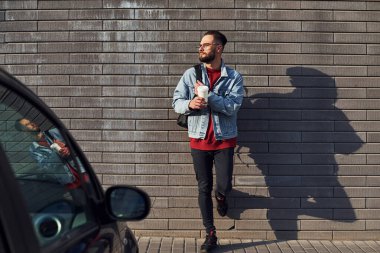 Gündüz vakti elektrikli ayakkabıyla dışarıda dikilen, günlük kıyafetli yakışıklı bir genç..