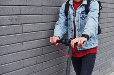 Close up view of guy in casual clothes that riding electric schooter outdoors at sunny daytime.