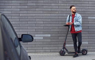 Gündüz vakti elektrikli ayakkabıyla dışarıda dikilen, günlük kıyafetli yakışıklı bir genç..
