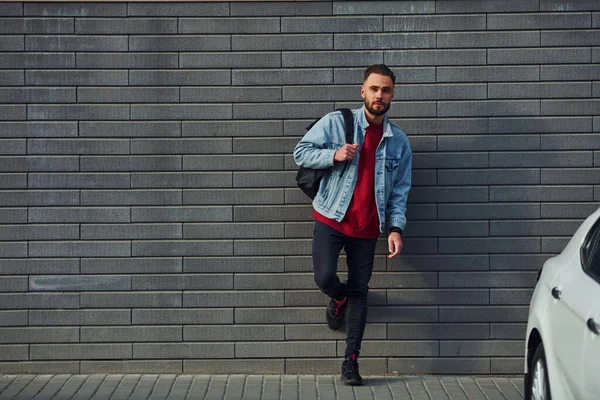 Günlük kıyafetlerle yakışıklı genç adam güneşli bir günde dışarıda, beyaz arabanın yanında..