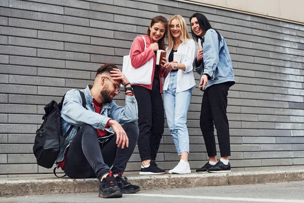 Üç kadın ayakta dikilip gülerken gündüz binanın yanında oturan adama..