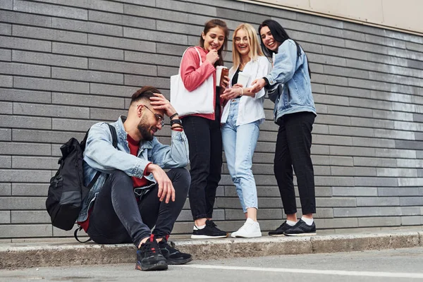 Üç kadın ayakta dikilip gülerken gündüz binanın yanında oturan adama..