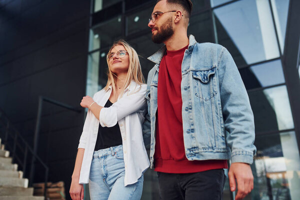 Young stylish man with woman in casual clothes outdoors together near business building. Conception of friendship or relationships.