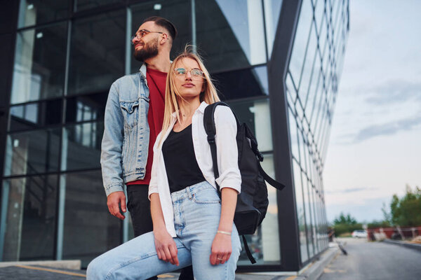 Young stylish man with woman in casual clothes outdoors together near business building. Conception of friendship or relationships.