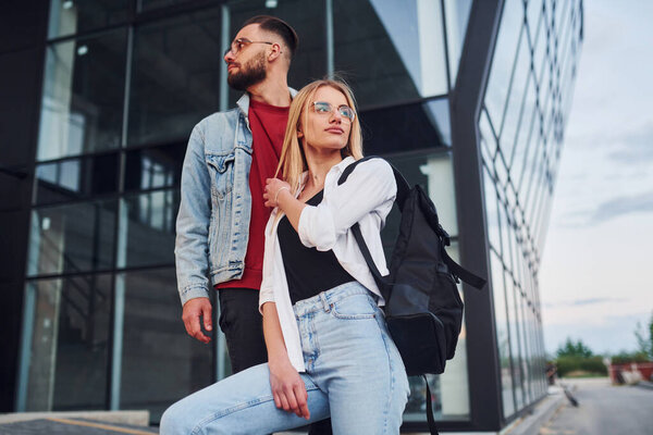 Young stylish man with woman in casual clothes outdoors together near business building. Conception of friendship or relationships.