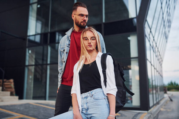 Young stylish man with woman in casual clothes outdoors together near business building. Conception of friendship or relationships.