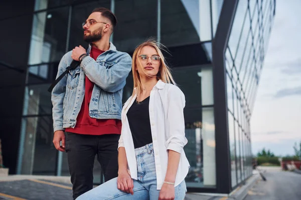 Young stylish man with woman in casual clothes outdoors together near business building. Conception of friendship or relationships.