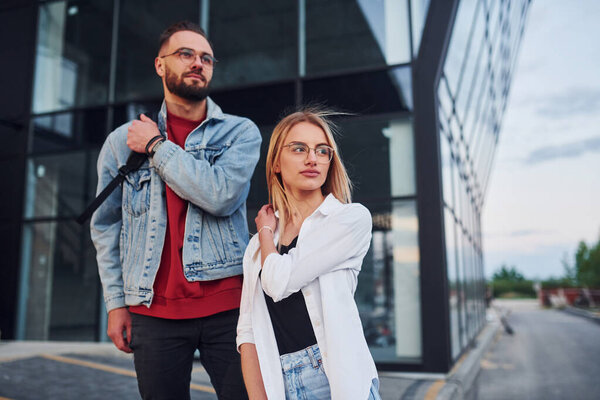 Young stylish man with woman in casual clothes outdoors together near business building. Conception of friendship or relationships.