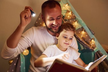 Kitap okumak ve el feneri kullanmak. Babası ve genç kızı çadırın yanında birlikte vakit geçiriyorlar..