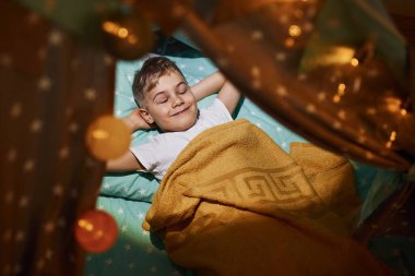 Geceleri çadırda uzanan günlük elbiseli genç bir çocuk..