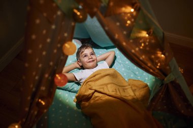 Geceleri çadırda uzanan günlük elbiseli genç bir çocuk..