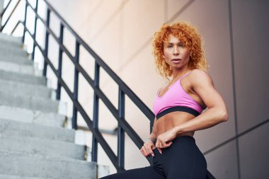 Spor kıyafetleri içinde genç Avrupalı kızıl kadın vücudunu gösteriyor ve spor egzersizlerinden sonra dışarıda poz veriyor..