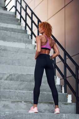 Spor kıyafetleri içinde genç Avrupalı kızıl kadın vücudunu gösteriyor ve spor egzersizlerinden sonra dışarıda poz veriyor..