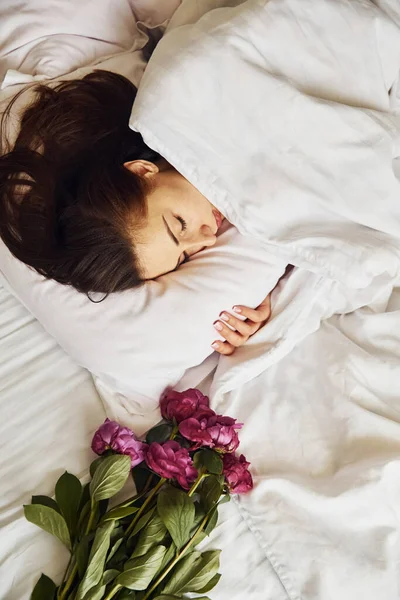 花とベッドの上に横になります 週末を家で一人で過ごす若い女性 — ストック写真