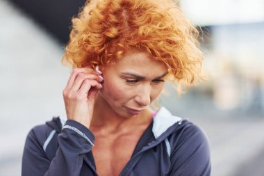 Kulaklıkla müzik dinliyorum. Açık havada duran genç Avrupalı kızıl saçlı kadının portresi..