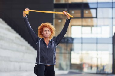 Avrupalı genç kızıl saçlı spor elbiseli kadın dışarıda halatla egzersiz yapıyor..