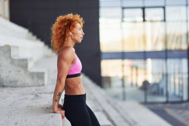 Avrupalı genç, kızıl saçlı, spor elbiseli, açık havada merdivenlerde duran..