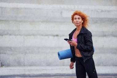 Avrupalı genç, kızıl saçlı, spor elbiseli, elinde telefon ve paspas olan bir kadın..