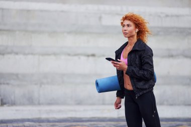 Avrupalı genç, kızıl saçlı, spor elbiseli, elinde telefon ve paspas olan bir kadın..