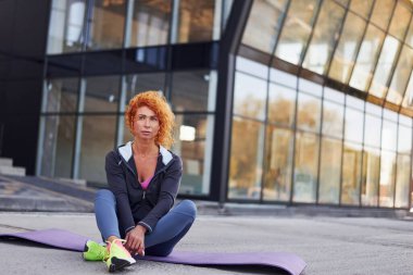 Genç Avrupalı kızıl saçlı spor elbiseli kadın dışarıda oturuyor..