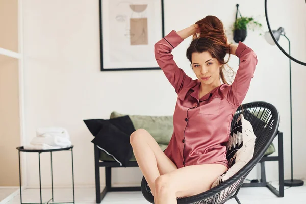 Sexy young woman in pink pajamas sitting on chair indoors at daytime.