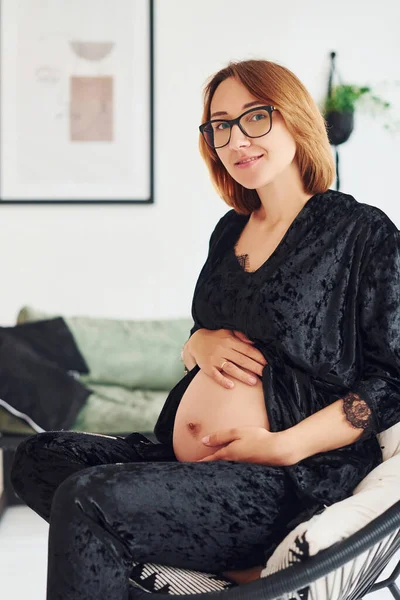 Zwangere Jonge Vrouw Bril Zwarte Pyjama Zitten Binnen Overdag — Stockfoto