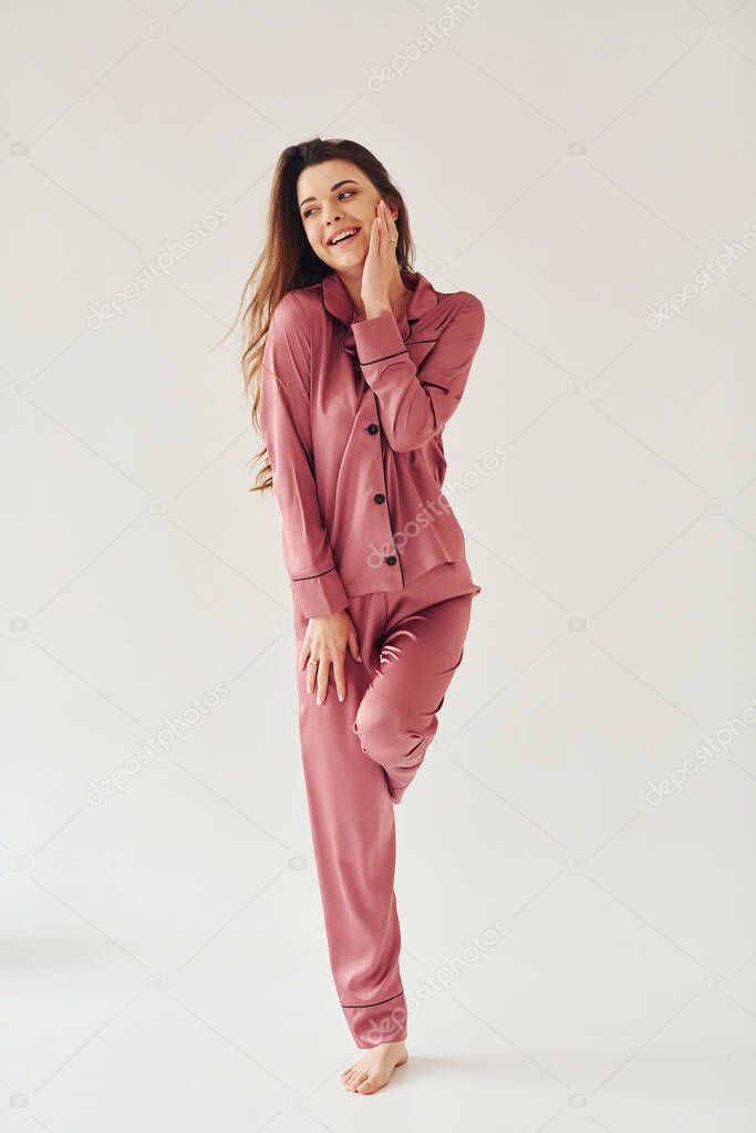 Cheerful young woman in pajamas standing indoors against white background in the studio.