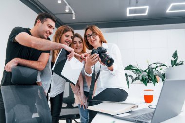 Ofiste resmi giyinmiş bir grup iş adamı kameradaki fotoğraflara bakıyor..