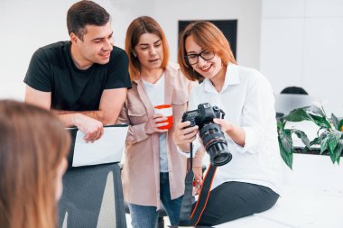 Ofiste resmi giyinmiş bir grup iş adamı kameradaki fotoğraflara bakıyor..