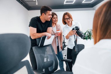 Ofiste resmi giyinmiş bir grup iş adamı kameradaki fotoğraflara bakıyor..