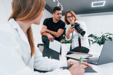 Ofiste resmi giyinmiş bir grup iş adamı kameradaki fotoğraflara bakıyor..