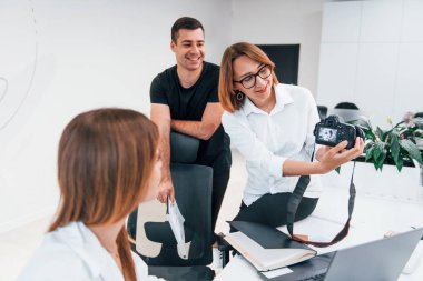 Ofiste resmi giyinmiş bir grup iş adamı kameradaki fotoğraflara bakıyor..