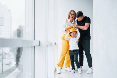 Sarı üniformalı kadın işçi, evde erkek ve çocukla dikiliyor..