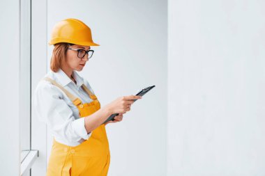 Elinde not defteriyle. Sarı üniformalı kadın işçi ya da mühendis ve içeride duran sert şapkalı..